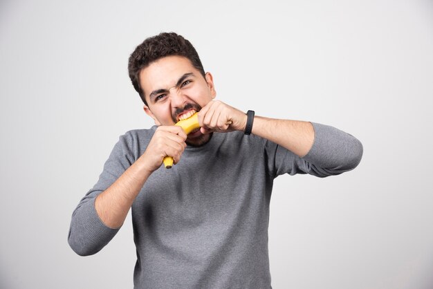 Um jovem comendo uma banana sobre uma parede branca.