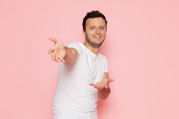 Um jovem do sexo masculino com camiseta branca e calça jeans posando e sorrindo na mesa rosa.