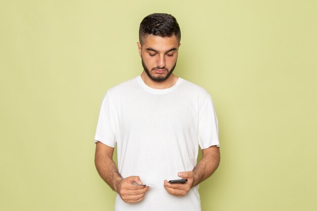 Um jovem do sexo masculino com camiseta branca segurando o telefone e o cartão