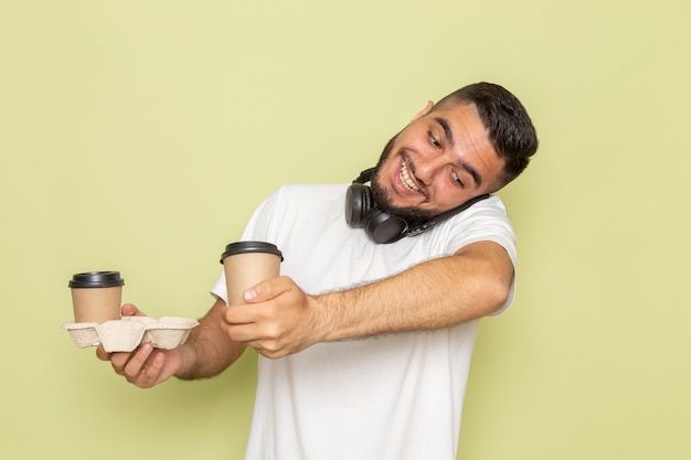 Foto grátis um jovem do sexo masculino com camiseta branca segurando xícaras de café enquanto fala ao telefone