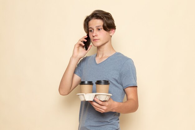 Um jovem do sexo masculino com camiseta cinza segurando xícaras de café e falando ao telefone