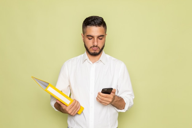 Um jovem do sexo masculino de camisa branca segurando arquivos amarelos e usando seu telefone