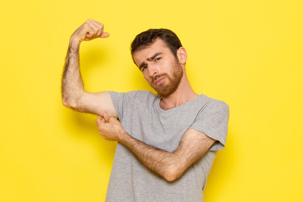 Um jovem do sexo masculino em uma camiseta cinza flexionando na parede amarela homem cor modelo emoção roupas