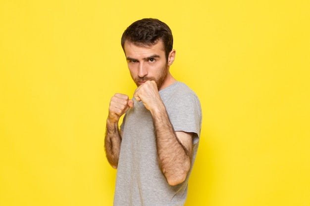 Um jovem do sexo masculino em uma camiseta cinza posando com um estande de boxe na parede amarela homem expressão emoção cor modelo
