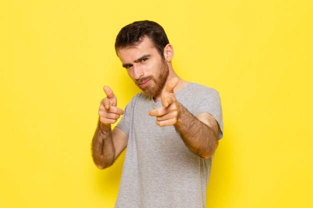 Um jovem do sexo masculino em uma camiseta cinza posando na parede amarela modelo de cor de expressão de emoção de homem