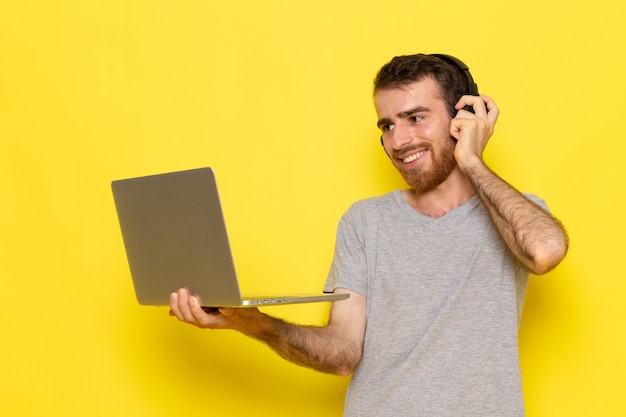 Um jovem do sexo masculino em uma camiseta cinza usando um laptop com um sorriso na parede amarela modelo de cor emoção expressão de homem