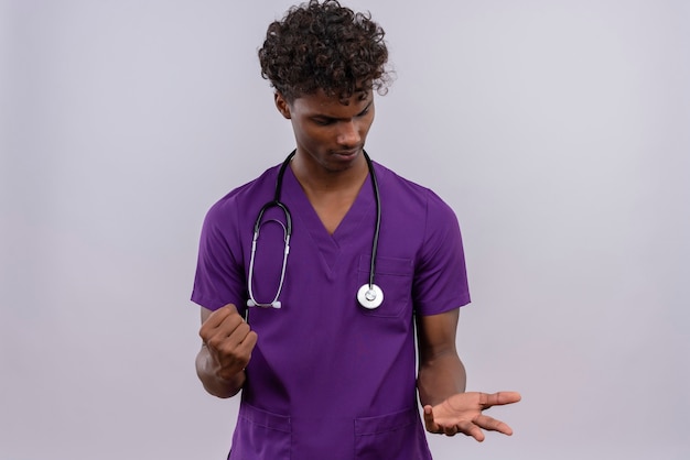 Um jovem e confuso médico atraente, de pele escura, cabelo encaracolado, usando uniforme violeta com estetoscópio levantando as mãos com o punho cerrado