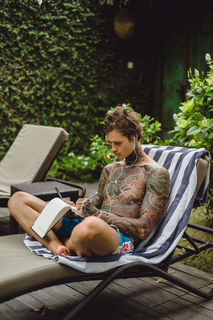 Um jovem em tatuagens usando fones de ouvido ouve música e desenha em um notebook.