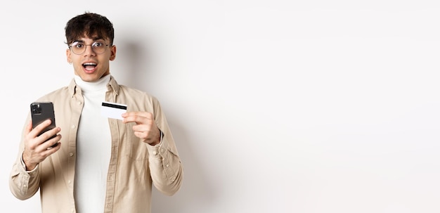 Foto grátis um jovem empolgado fazendo compras on-line segurando um telefone celular e um cartão de crédito plástico fazendo compras em