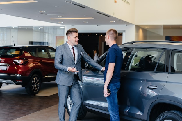 Um jovem empresário com um vendedor olha para um carro novo em uma concessionária. comprando um carro.