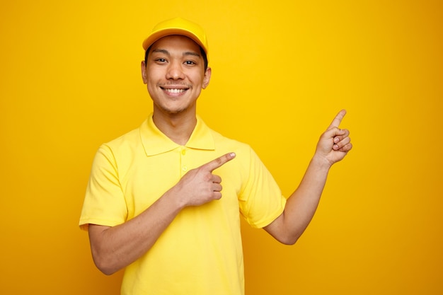 Um jovem entregador sorridente vestindo um boné e um uniforme apontando para a esquina.