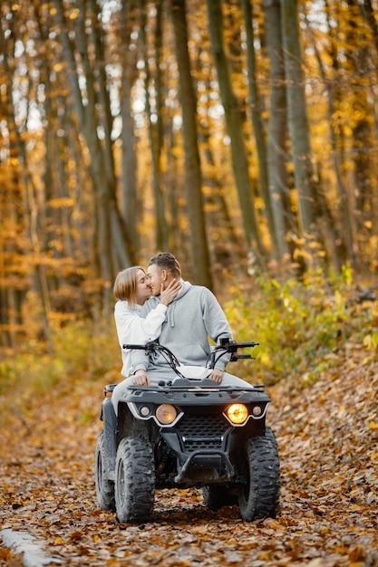 Um jovem homem caucasiano e uma mulher andando de quadriciclo atv na floresta de outono lindo casal beijando casal vestindo trajes esportivos cinza