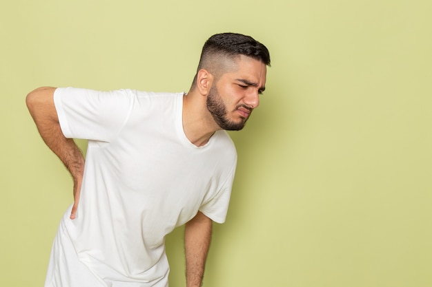 Um jovem homem de camiseta branca com forte dor nas costas, vista frontal