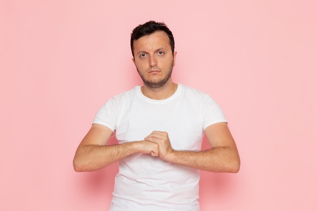 Um jovem homem de frente para uma camiseta branca e calça jeans posando de maneira agressiva na mesa rosa.