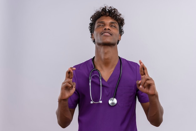 Um jovem médico bonito de pele escura com cabelo encaracolado e uniforme violeta com estetoscópio segurando o dedo e sentindo-se relaxado