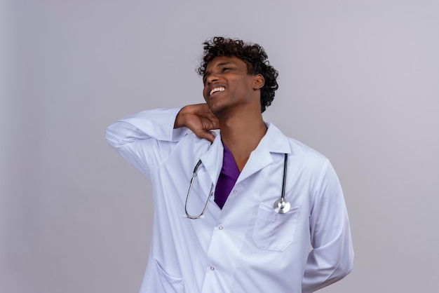 Um jovem médico bonito de pele escura com cabelo encaracolado, jaleco branco e estetoscópio com dor de cabeça