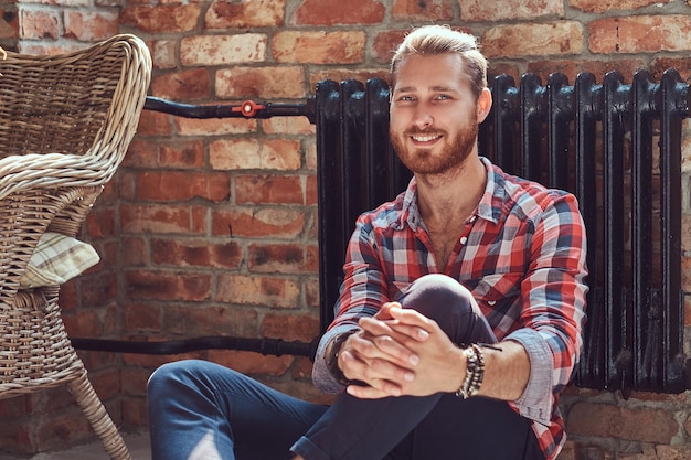 Um jovem sorridente bonito ruiva modelo homem senta-se em um balanço na sala com um interior loft.