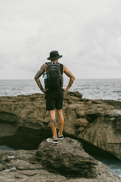 Foto grátis um jovem viajante com uma mochila no oceano nas rochas olha para a distância.