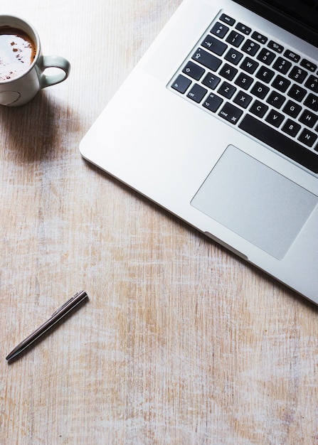 Um laptop aberto com xícara de café e caneta em fundo de madeira