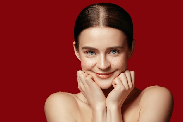 Foto grátis um lindo rosto feminino. pele perfeita e limpa de jovem caucasiana em fundo vermelho studio.