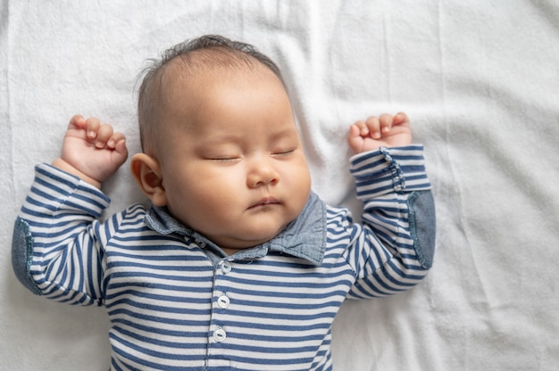 Um menino com uma camisa listrada está dormindo na cama.