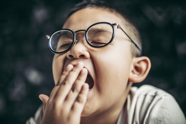 Um menino de óculos estudando e sonolento.