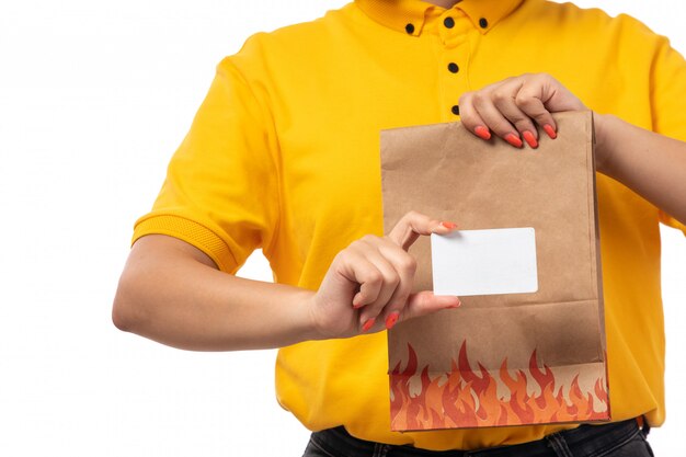 Um mensageiro feminino vista frontal na camisa amarela boné amarelo segurando o cartão branco e pacote com comida em branco