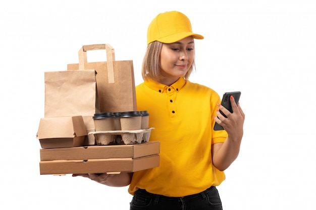 Foto grátis um mensageiro feminino vista frontal na camisa amarela boné amarelo sorrindo segurando smartphone e caixas em branco