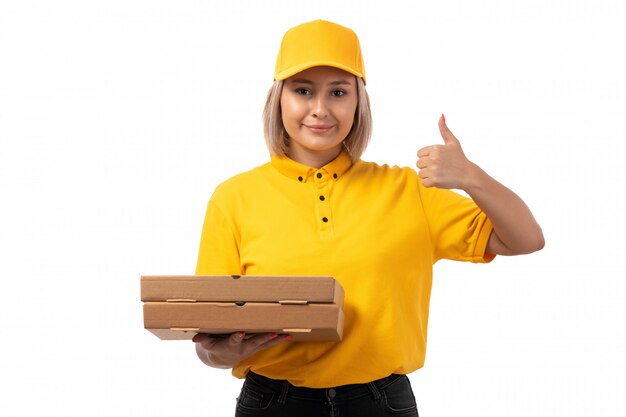 Um mensageiro feminino vista frontal na camisa amarela camisa amarela e calça jeans preta segurando caixas de pizza sorrindo mostrando como sinal em branco