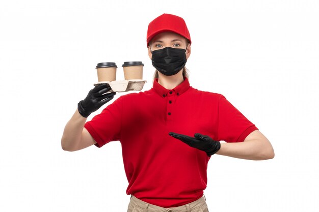Um mensageiro feminino vista frontal na camisa vermelha boné vermelho luvas pretas e máscara preta segurando café