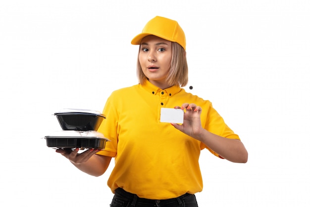 Um mensageiro feminino vista frontal no boné amarelo camisa amarela segurando o cartão branco e tigelas com comida em branco
