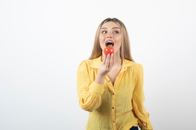 um modelo de jovem em pé e comendo um tomate vermelho.