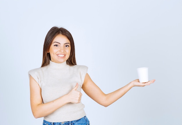 Foto grátis um modelo de mulher feliz segurando um copo de plástico e mostrando um polegar.