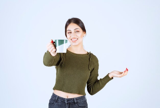 Um modelo de mulher jovem e bonita oferecendo um copo de bebida quente e olhando para a câmera.