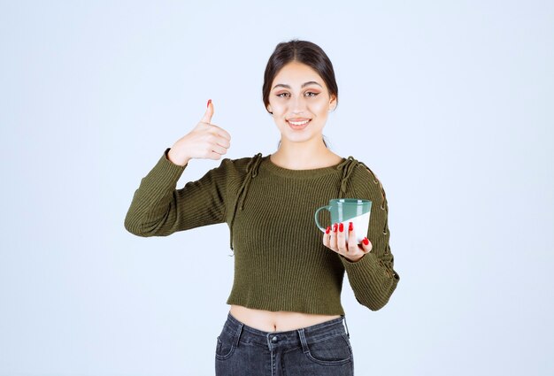 Um modelo de mulher jovem e bonita segurando um copo de bebida quente e mostrando o polegar.