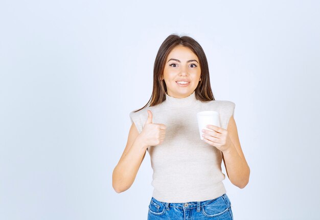 Um modelo de mulher sorridente segurando um copo de plástico e mostrando um polegar para cima.