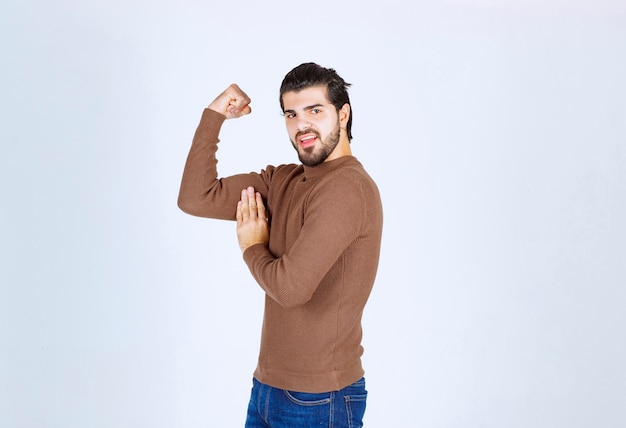Um modelo jovem e simpático em pé e mostrando seus bíceps sobre uma parede branca. Foto de alta qualidade