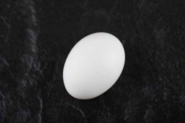 Um ovo de galinha branco fresco em uma mesa preta.