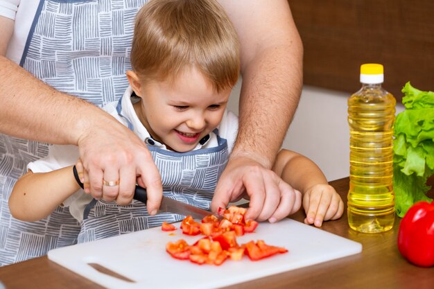 Um pai feliz e um filho pequeno preparam uma salada com legumes na cozinha.