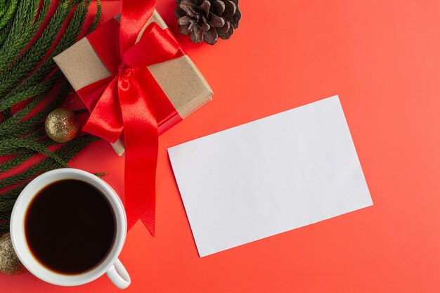 Um papel branco em branco, uma xícara de café e uma caixa de presente no chão vermelho