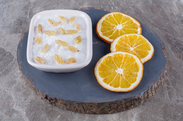 Um pedaço de madeira de mingau de aveia saudável com passas e fatias de frutas de laranja.