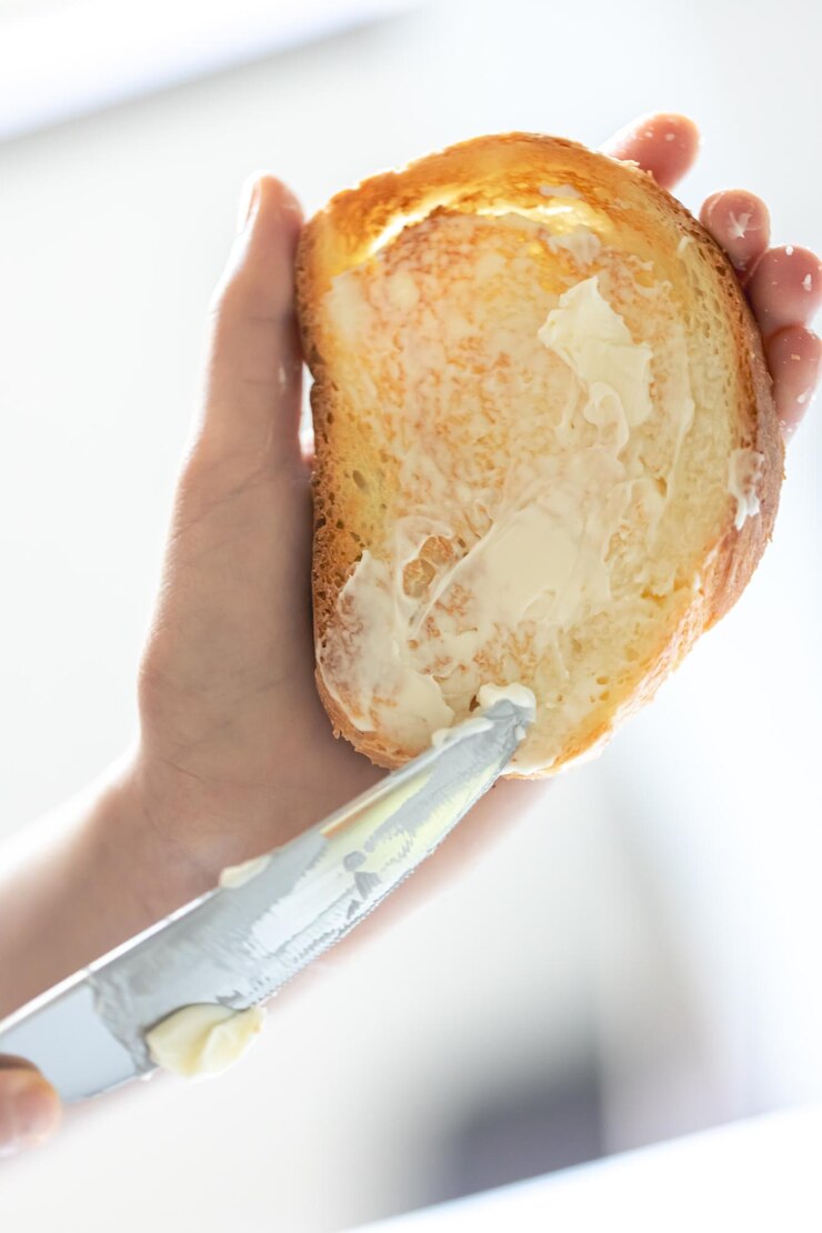 Foto grátis um pedaço de pão com manteiga na mão de uma mulher