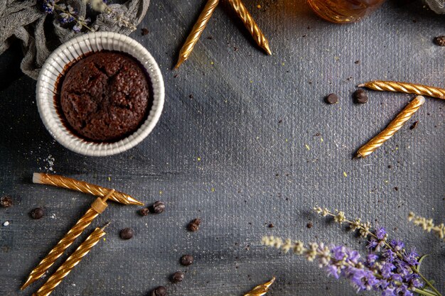 Um pequeno bolo de chocolate com velas e flores roxas e chá na mesa cinza.