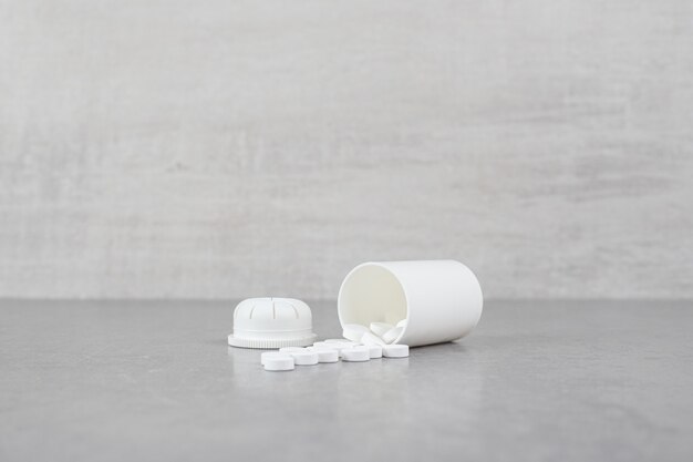 Um pequeno frasco branco de comprimidos brancos na superfície cinza