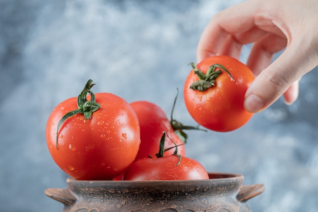 Um pote antigo com tomates frescos em uma parede cinza.