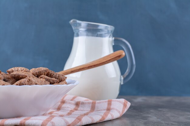 Um pote de leite com um prato branco cheio de cereais saudáveis.