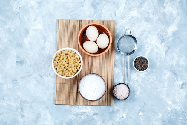 Um pouco de macarrão cavatappi com ovos, iogurte, especiarias, peneira em uma tigela no fundo cinza sujo e placa de corte, vista superior.