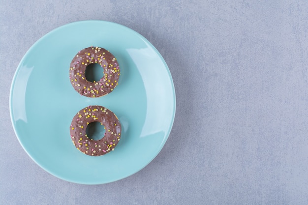 Um prato azul de deliciosos donuts de chocolate com granulado colorido.