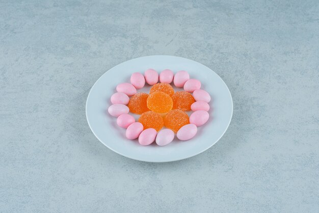Um prato branco cheio de balas de geleia de laranja e balas rosa