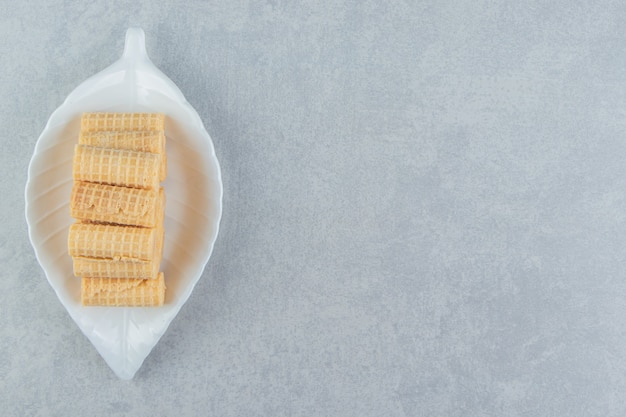 Um prato branco cheio de rolos de waffle crocantes.